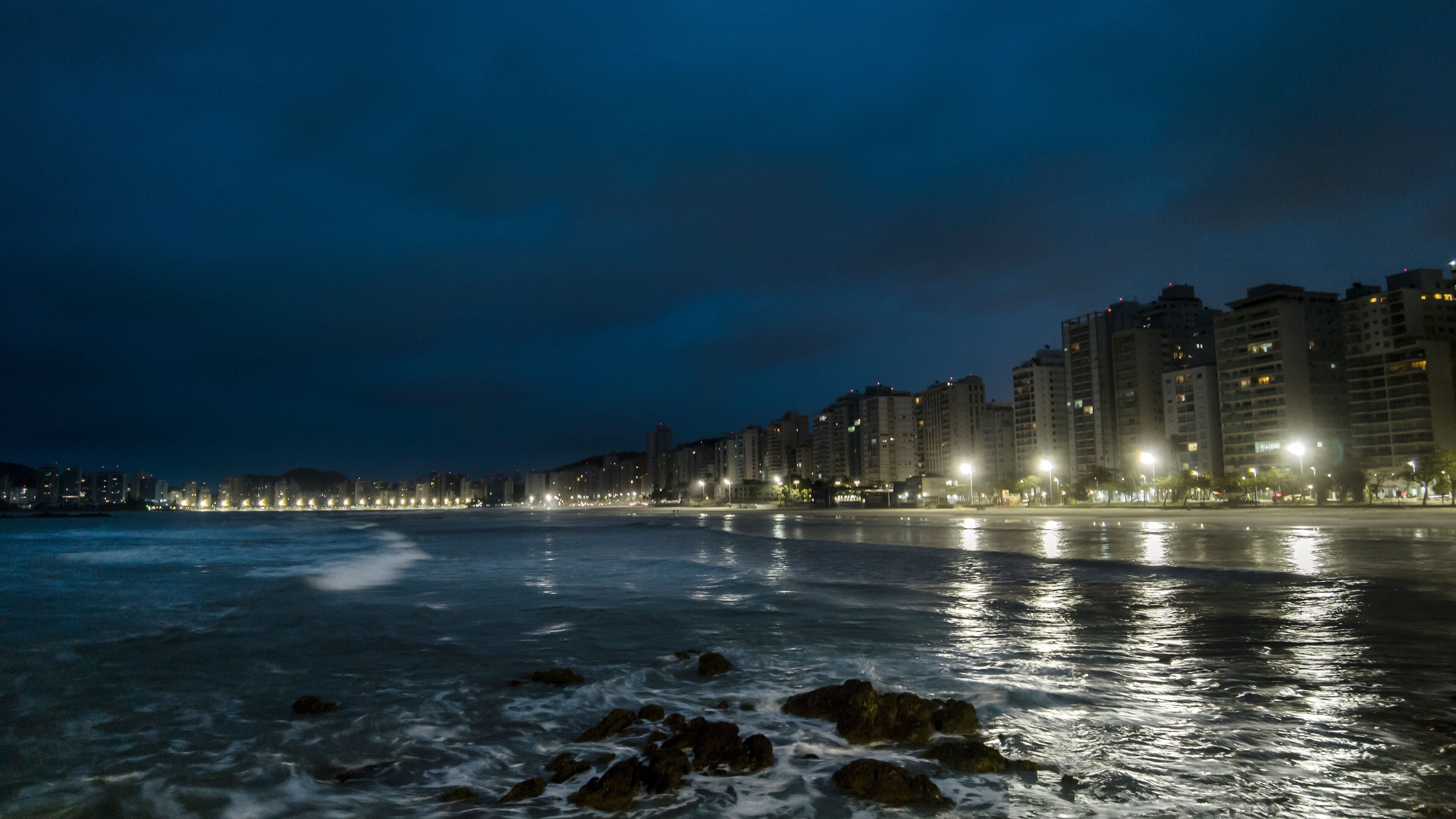 Night view of sea rocks with the background of Pitangueiras Beach with avenue and rise apartments na cidade de Guaruja, Sao Paulo state coast