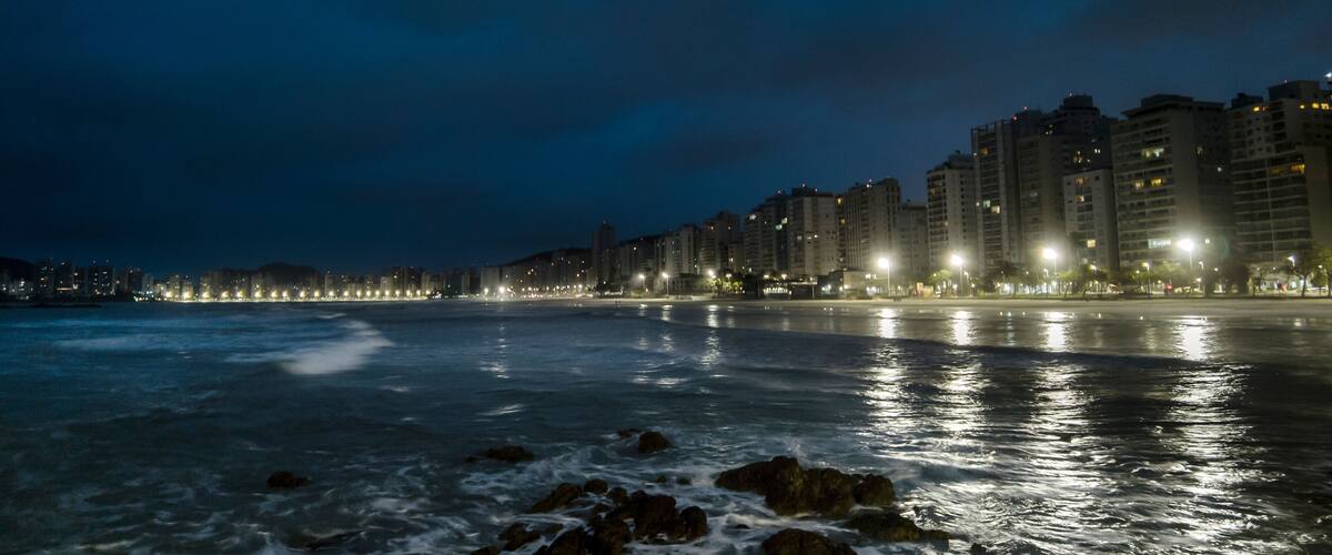 Night view of sea rocks with the background of Pitangueiras Beach with avenue and rise apartments na cidade de Guaruja, Sao Paulo state coast