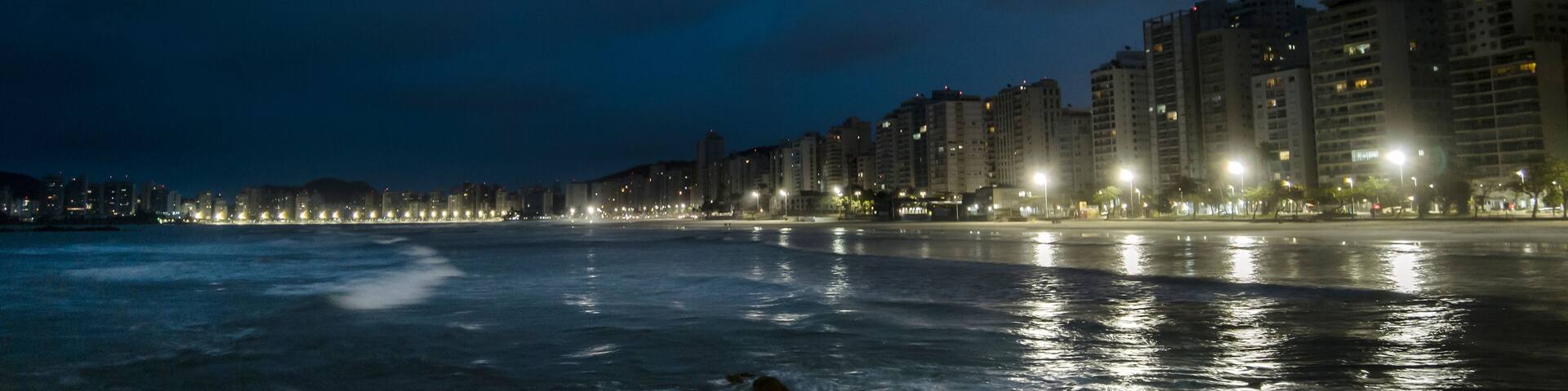 Night view of sea rocks with the background of Pitangueiras Beach with avenue and rise apartments na cidade de Guaruja, Sao Paulo state coast