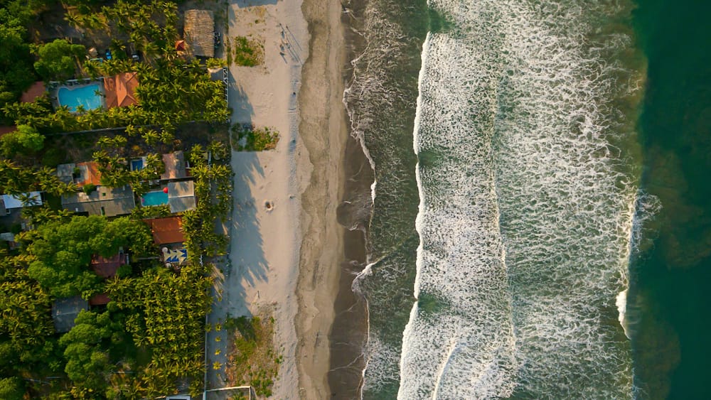 A beach with waves, a pool, and houses.