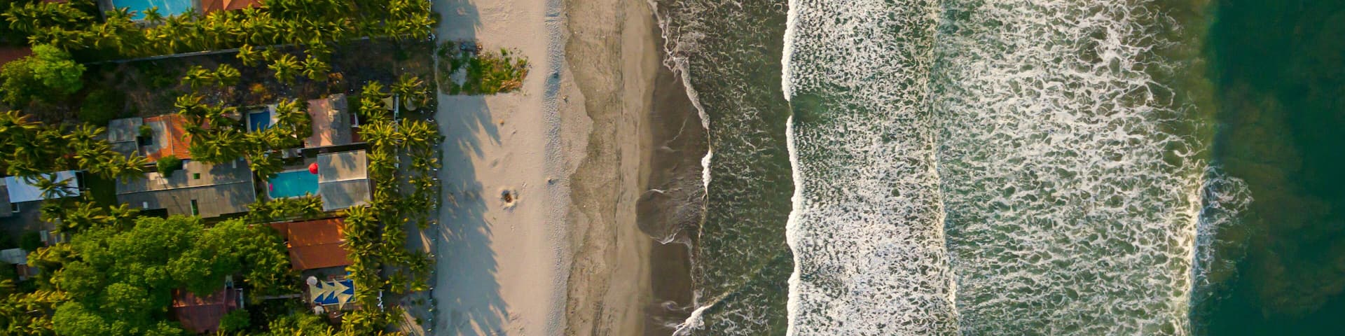 A beach with waves, a pool, and houses.