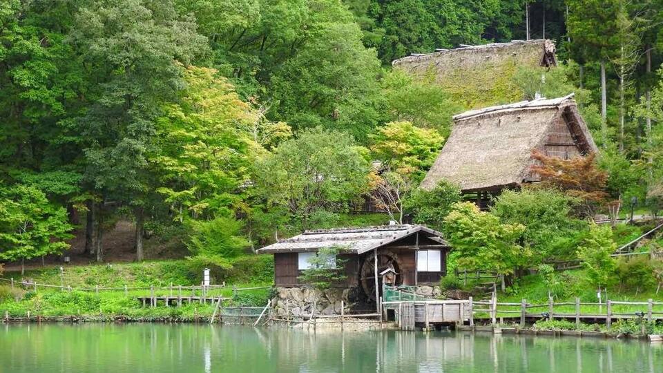 A traditional Japanese structure by a calm lake surrounded by lush greenery.