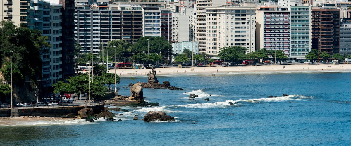 Un paysage urbain côtier avec de hauts immeubles, une plage de sable et des affleurements rocheux dans l’eau.