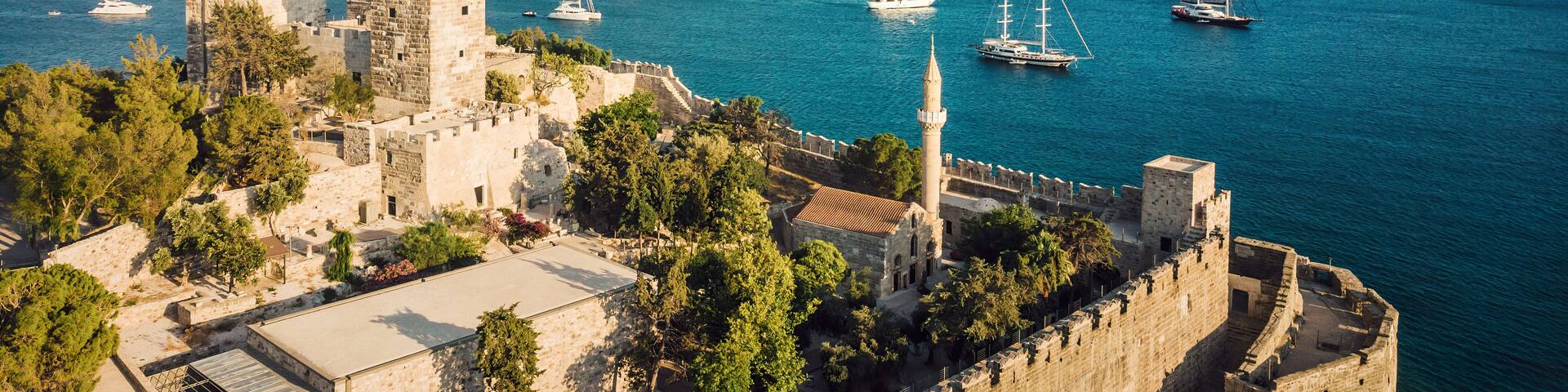 A coastal town with historic stone buildings, a castle, and a harbor with sailboats.