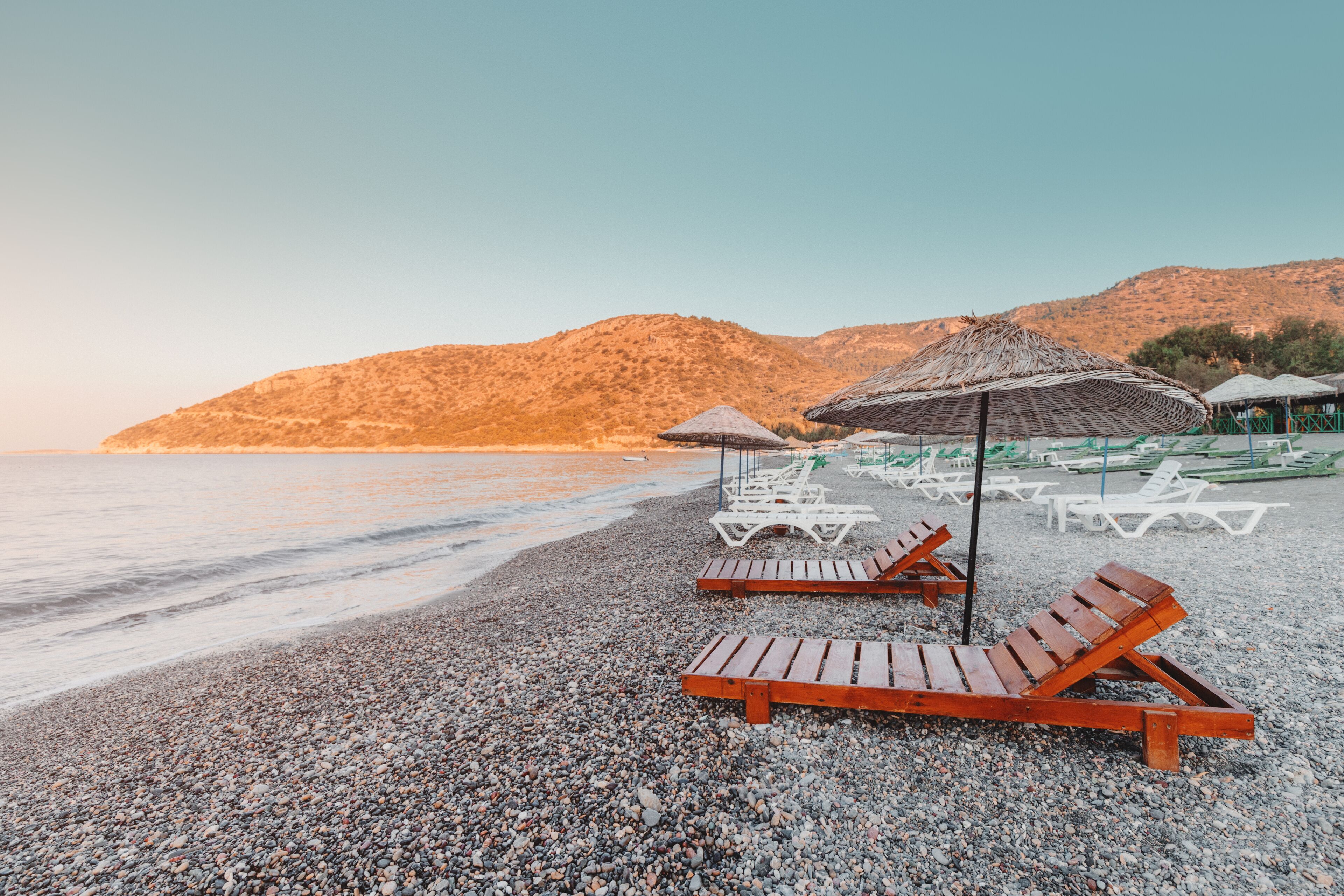 Sunbeds and sun umbrellas await vacationers on the shingle beach at Ovabuku beach on the Datca Peninsula in Turkey. The photo was taken in the early morning at sunrise