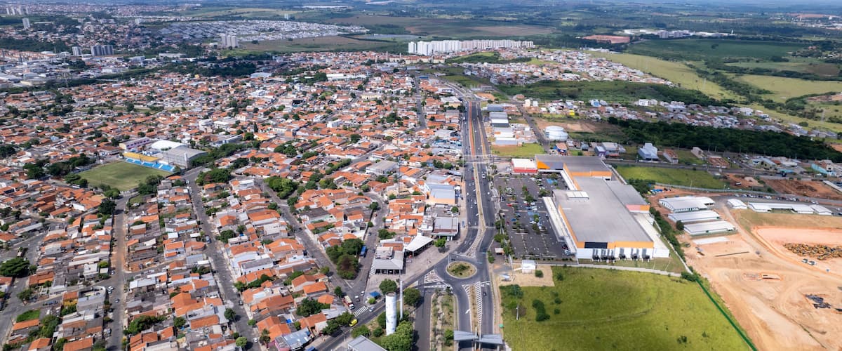 Vista aérea de una zona urbana densamente poblada con una mezcla de edificios residenciales y comerciales, una autopista destacada y campos verdes circundantes.