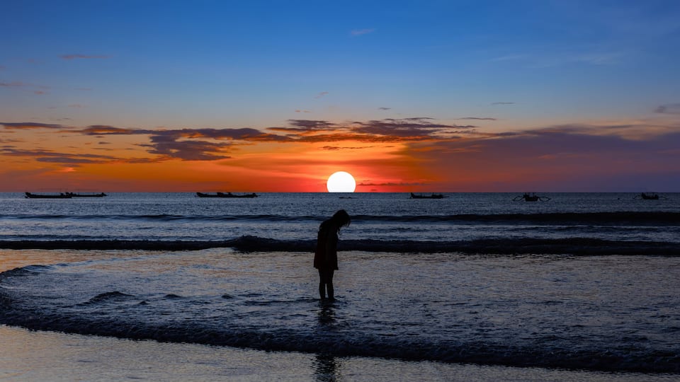 Beautiful colourful sunset on Kuta Beach on the island of Bali blue purple orange skies with turquoise blue waters and silhouette of people on the sandy beach the land of gods Bali Island Indonesia