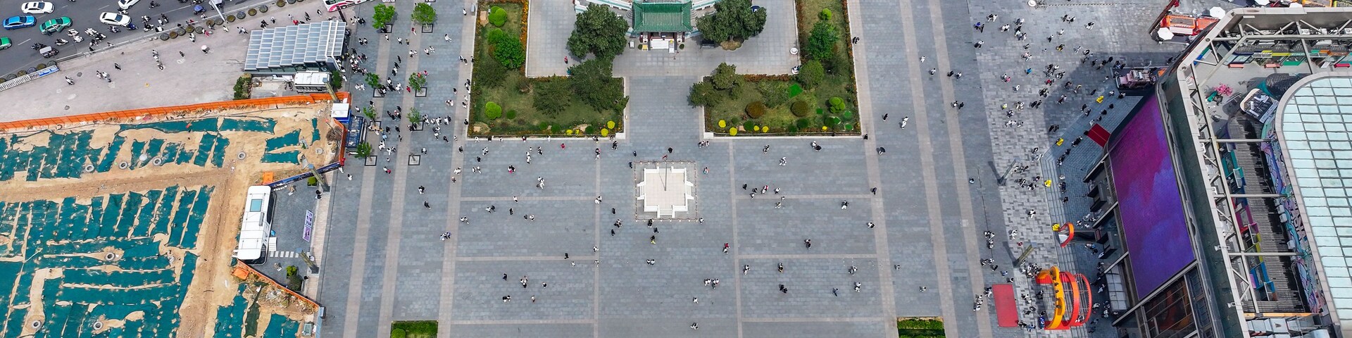 Uma grande praça aberta com um edifício peculiar que lembra um pagode, cercada por ruas e edifícios modernos.