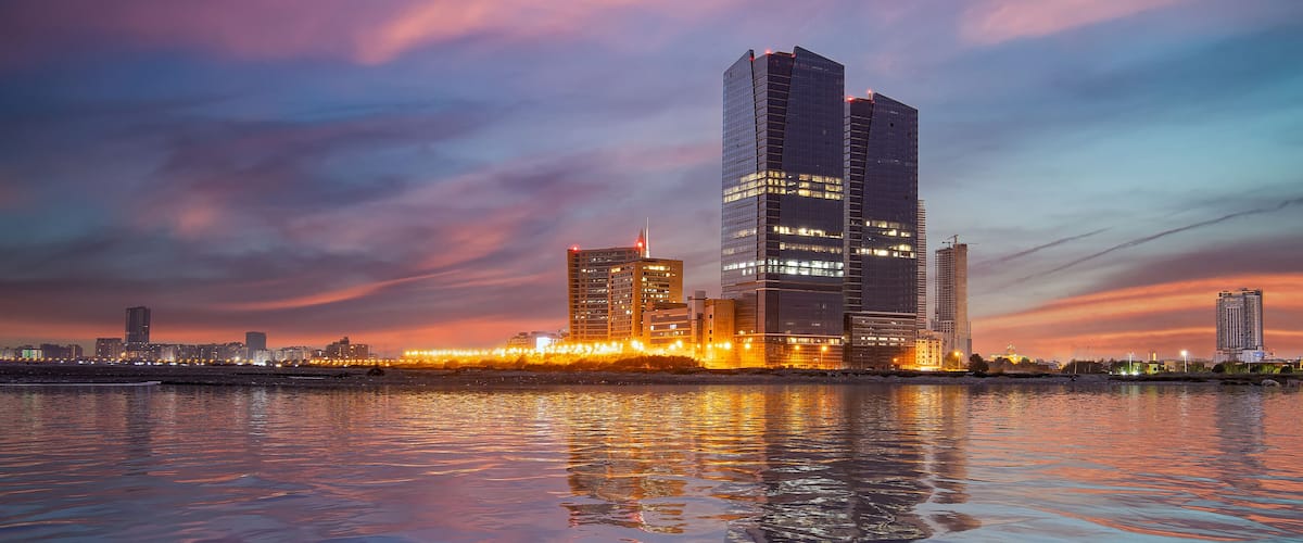 Une vue sur les gratte-ciel d’une ville, avec les bâtiments illuminés qui se reflètent sur l’eau au crépuscule.