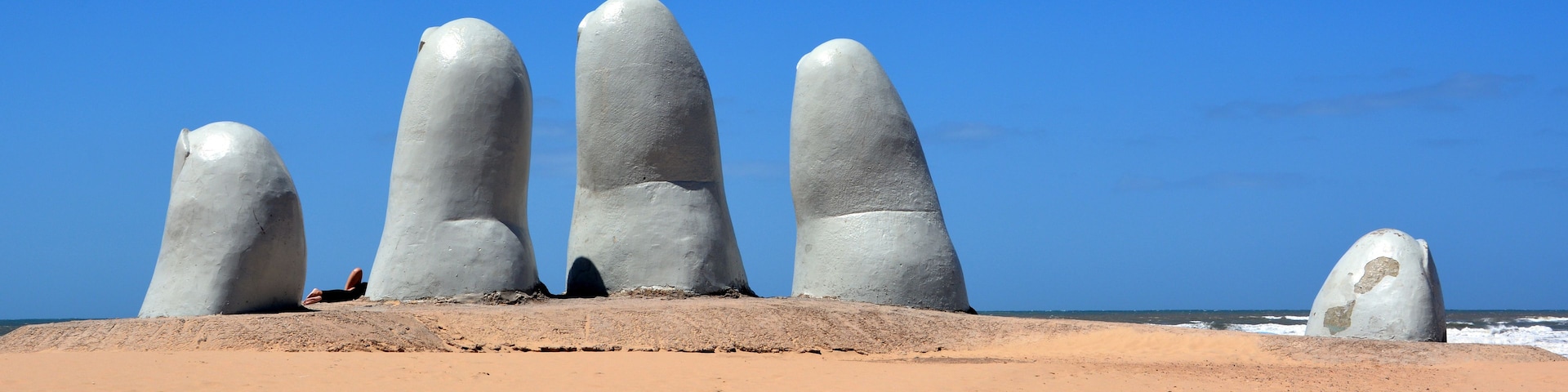 Uma praia arenosa com cinco grandes formações rochosas brancas e lisas que se assemelham a dedos.