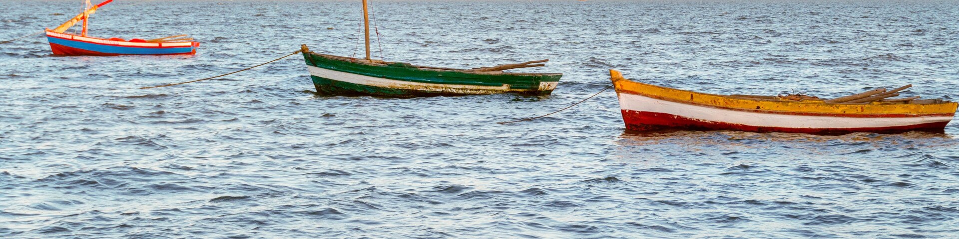 Tres pequeñas embarcaciones ancladas en aguas tranquilas, con un barco distante en el horizonte.