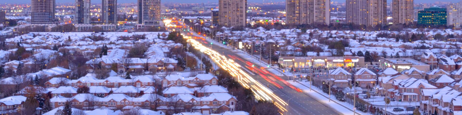Ariel view of snow covered rooftops of north american neighborhood houses in Mississauga, Ontario, Canada. Light trails of head and tail lights cars going on the highway in the evening