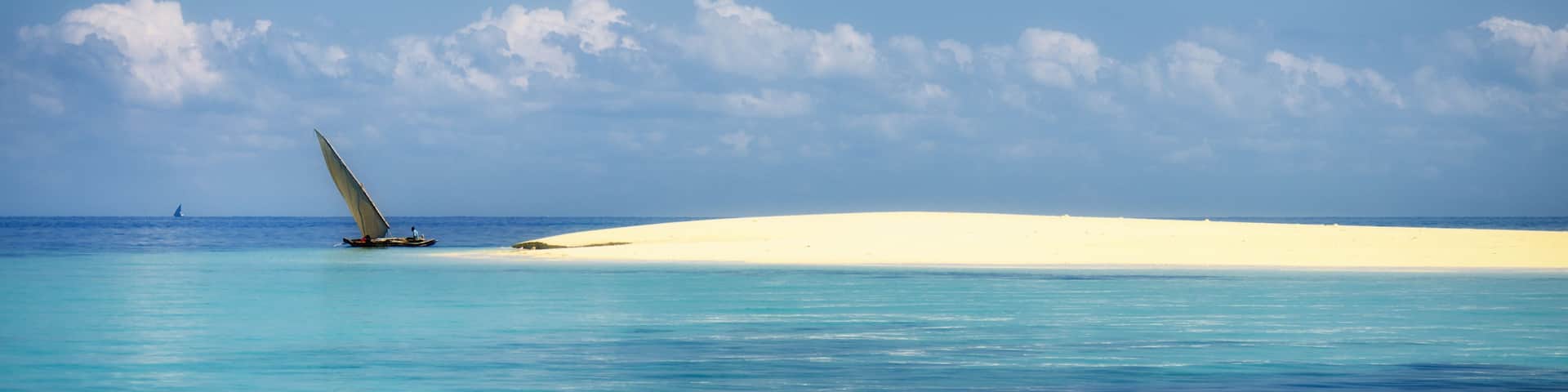 A sailboat on turquoise waters with a sandy beach and a clear sky.