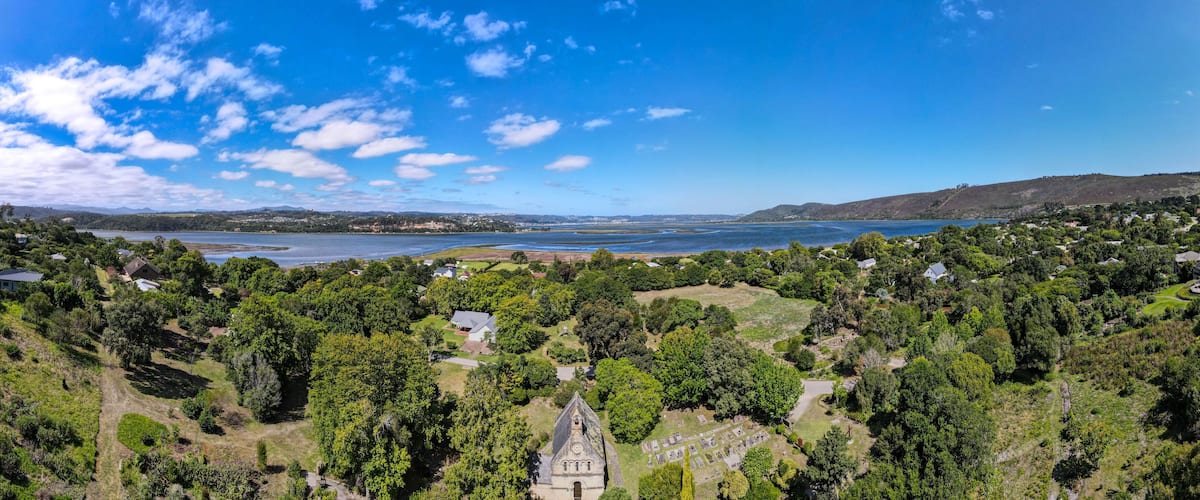 A coastal landscape with a church, dense greenery, and a clear blue sky.