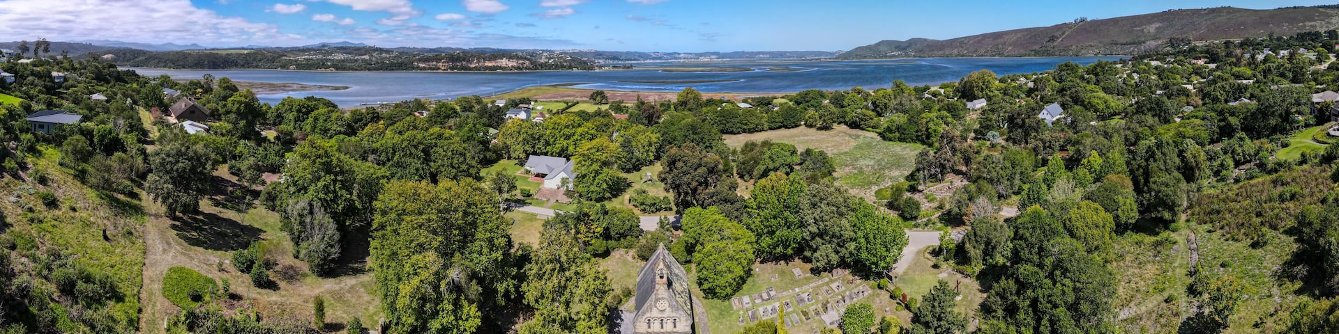 A coastal landscape with a church, dense greenery, and a clear blue sky.
