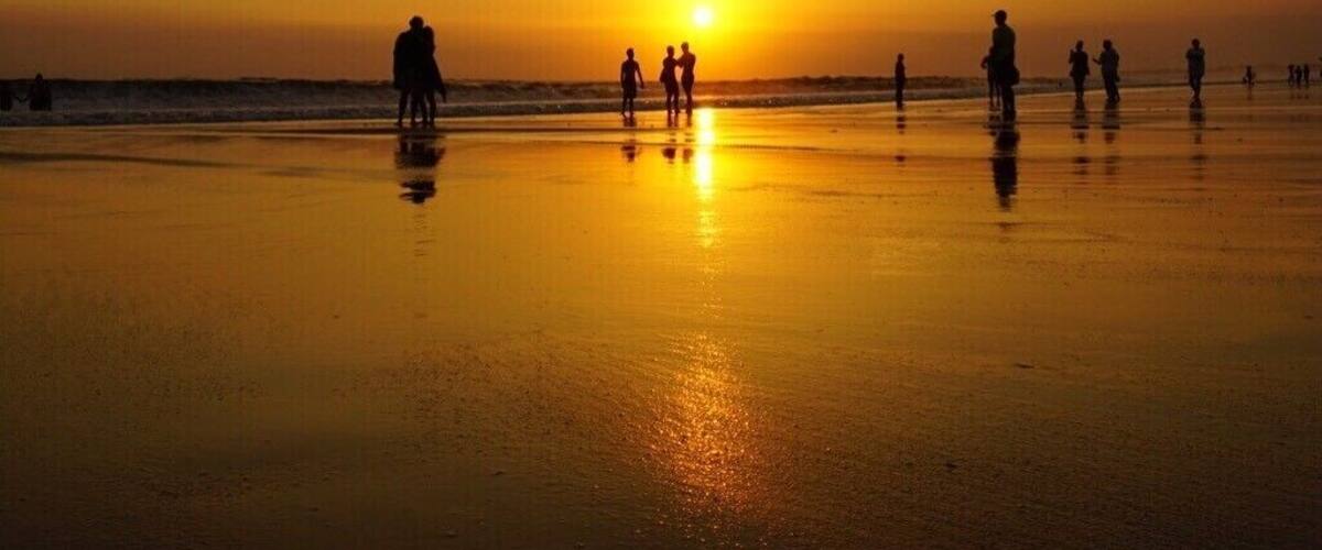 A beach at sunset with people walking along the shore.