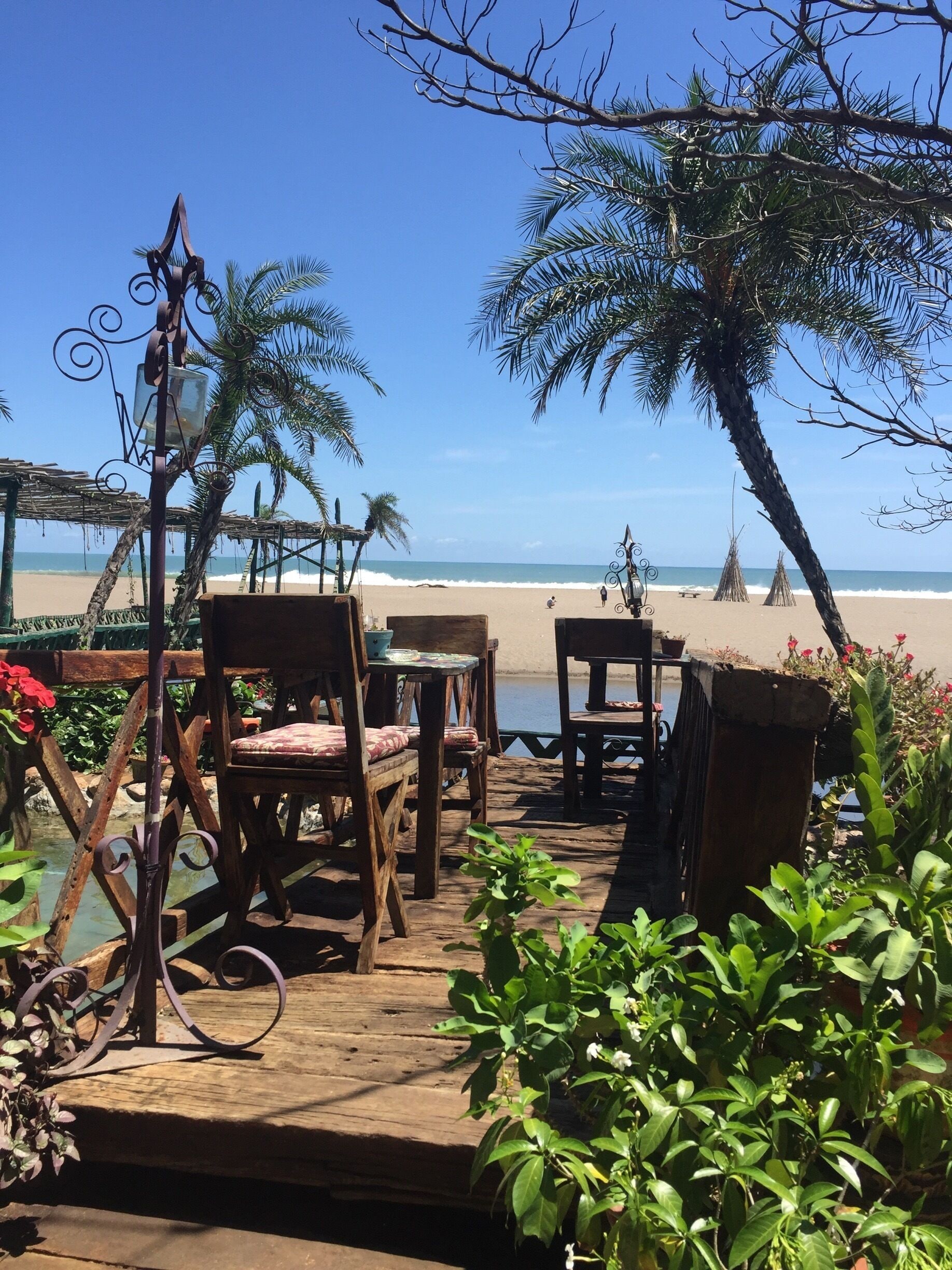 A wooden deck with chairs and tables overlooking a beach.