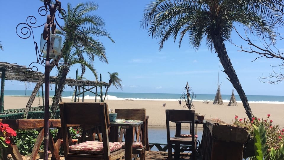 A wooden deck with chairs and tables overlooking a beach.