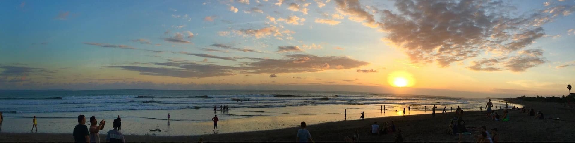 A beach at sunset with people walking and sitting on the sand.
