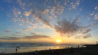 A beach at sunset with people walking and sitting on the sand.