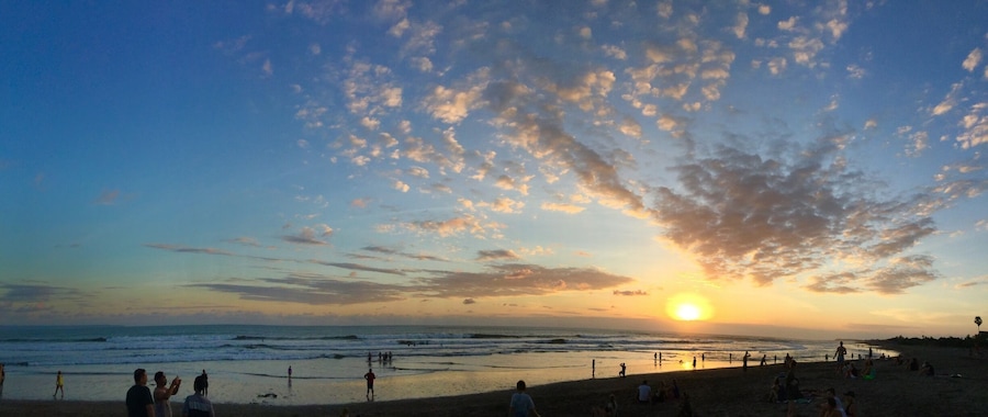 Una playa al atardecer con gente caminando y sentada en la arena.