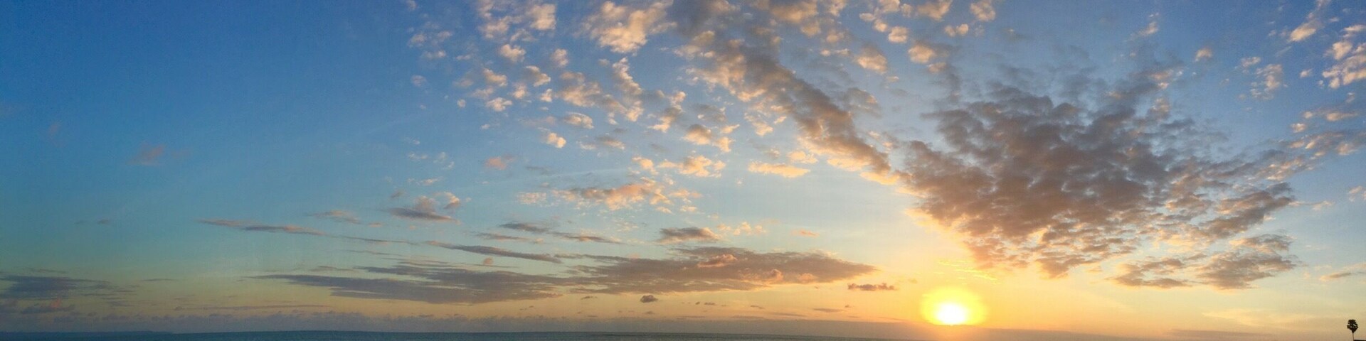 A beach at sunset with people walking and sitting on the sand.