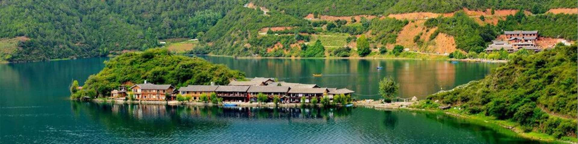A lakeside resort with buildings on stilts, surrounded by lush green hills and a calm lake.