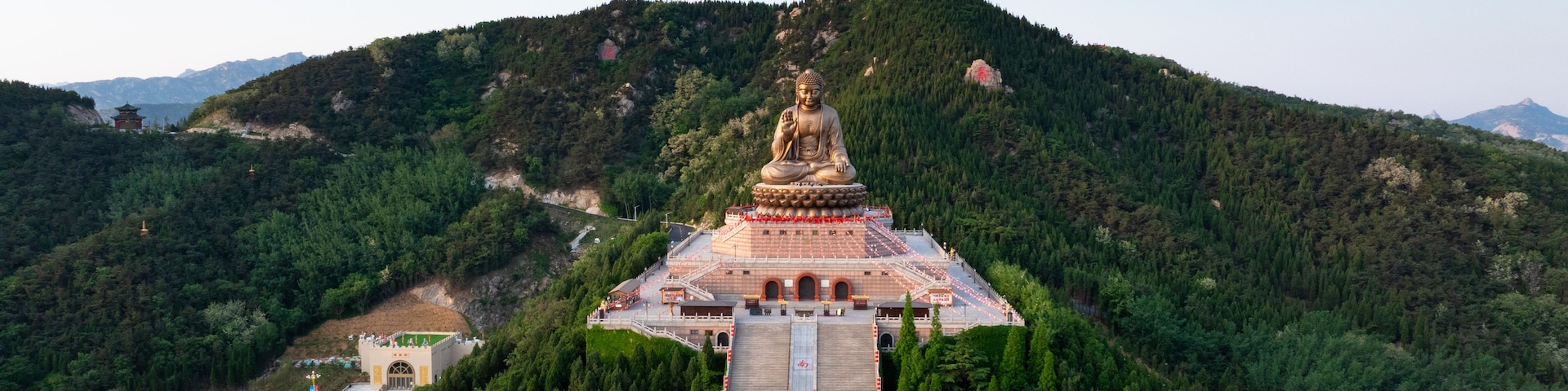 Uma grande estátua de Buda numa montanha, com uma estrada pavimentada que a leva até lá.