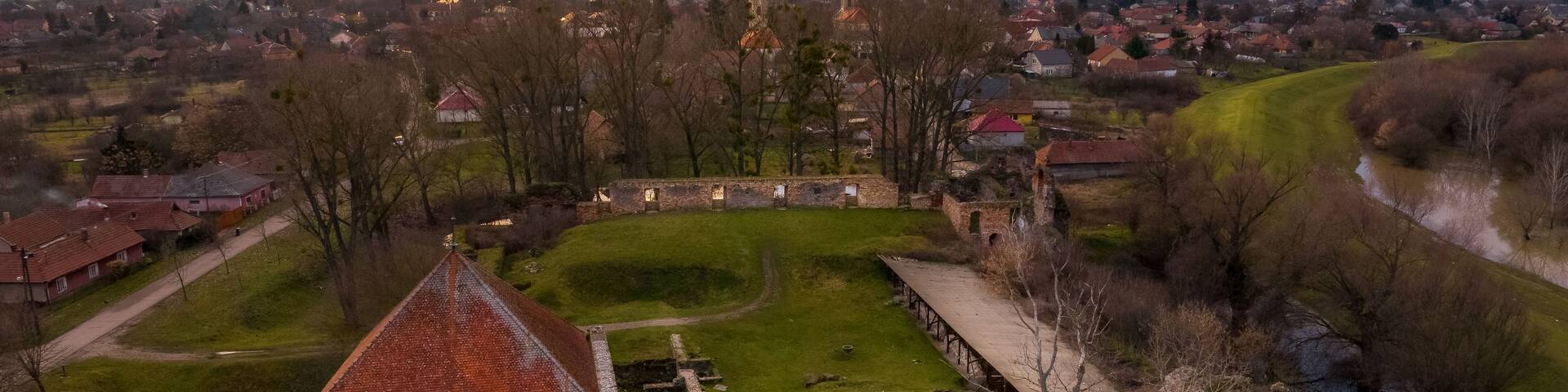 A historic castle surrounded by a moat, with a church in the background and a town across the river.