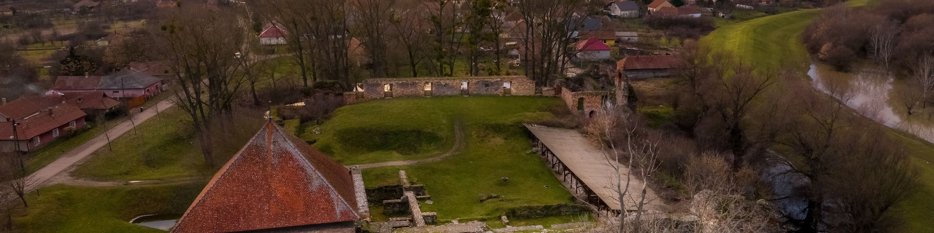 Um castelo histórico cercado por um fosso, com uma igreja ao fundo e uma cidade do outro lado do rio.