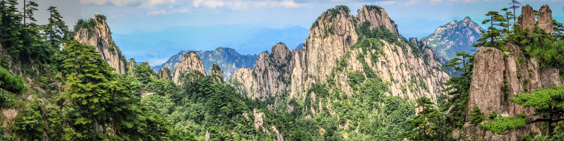 Panorama with pine trees in the foreground and rough rocky peaks leading to the horizon in Huang Shan (黄山, Yellow Mountains) China