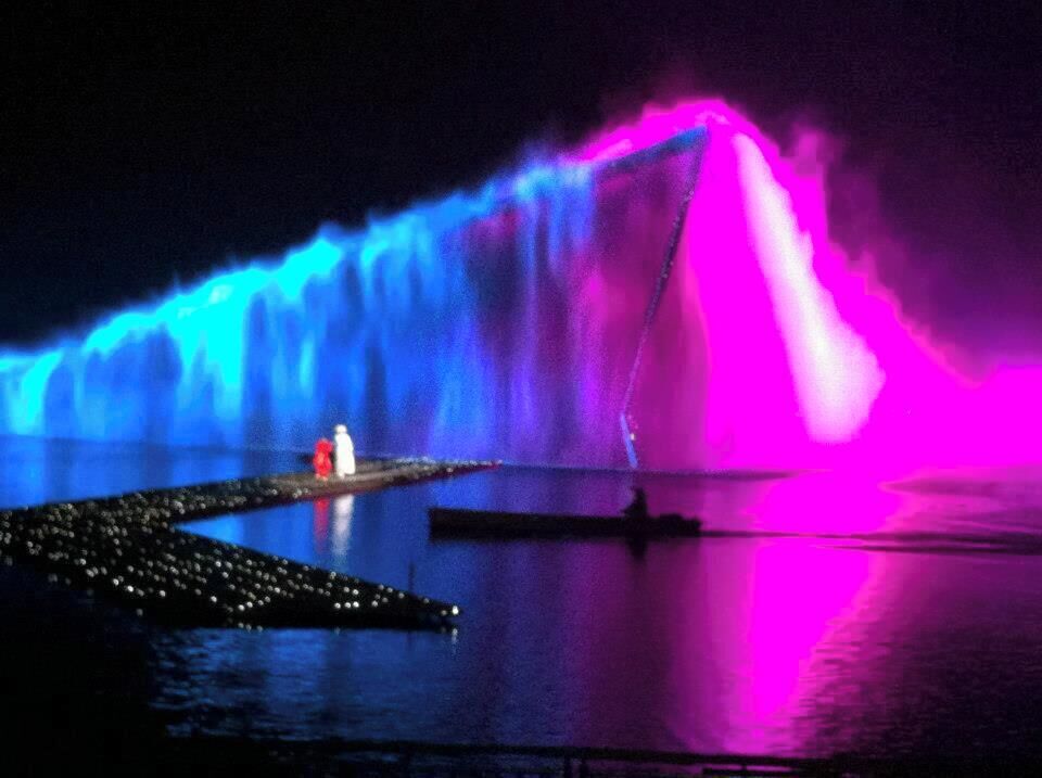 A nighttime water fountain with vibrant blue and pink lights.