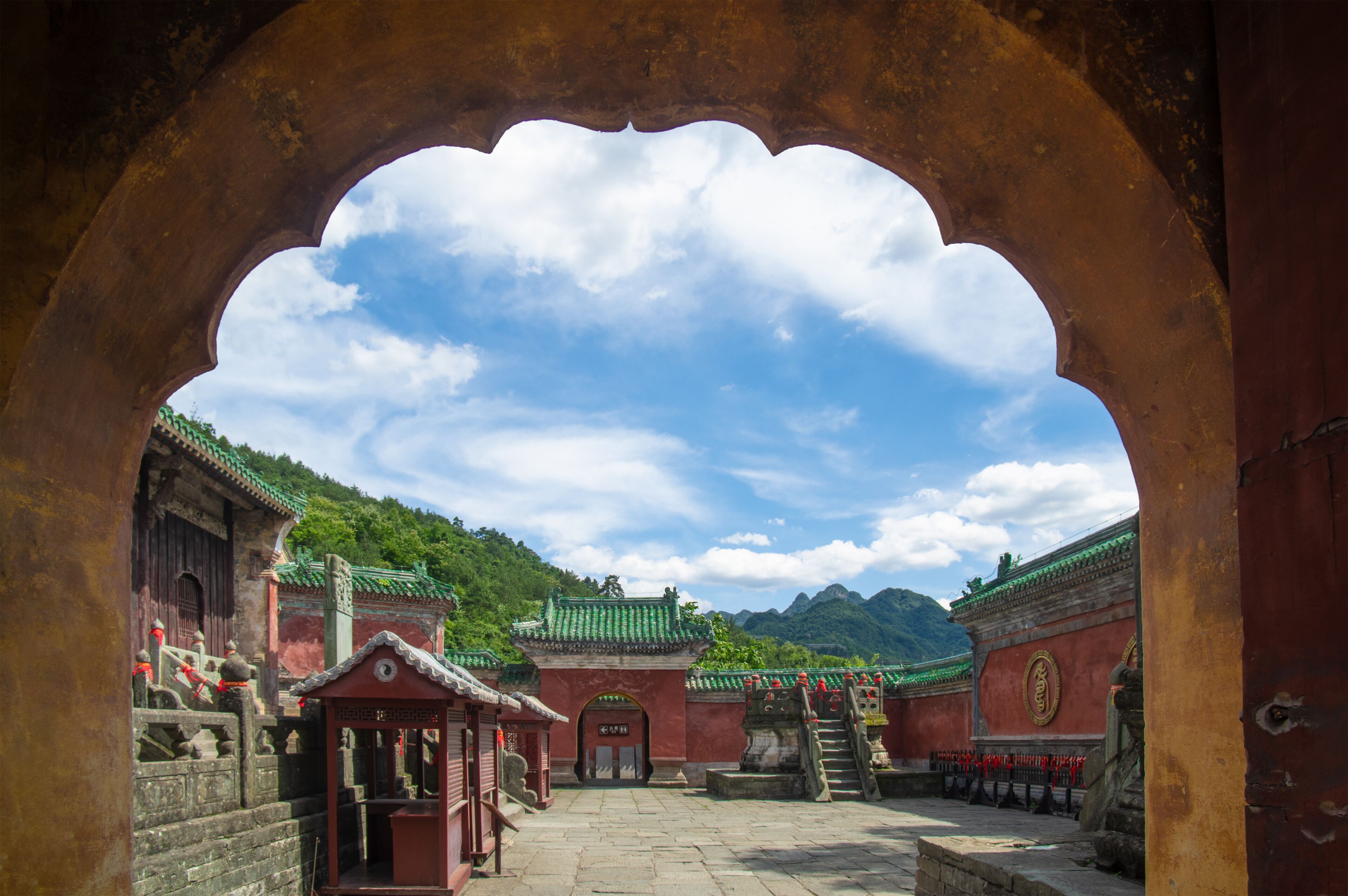 A traditional Chinese courtyard with a large archway, red walls, and green roofs.