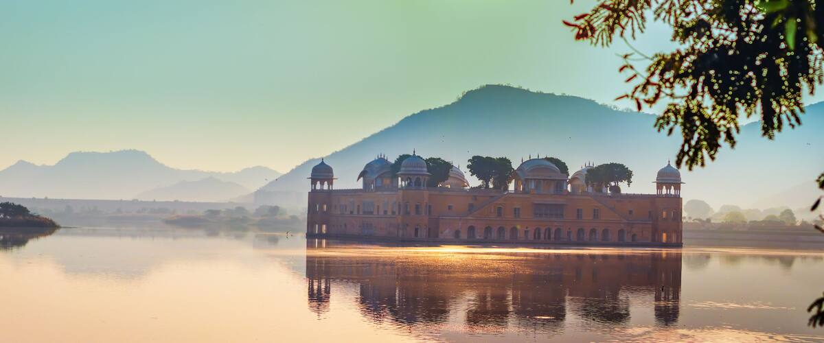 A serene lake with a reflection of a historic building with domes, surrounded by mountains and a clear sky.