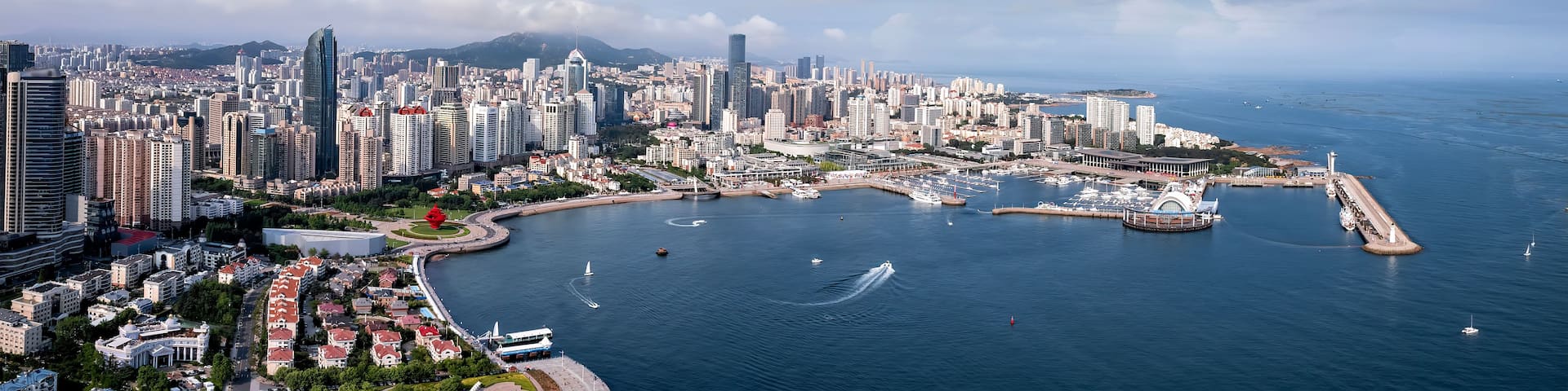 A coastal cityscape with high-rise buildings, a marina, and a clear sky.