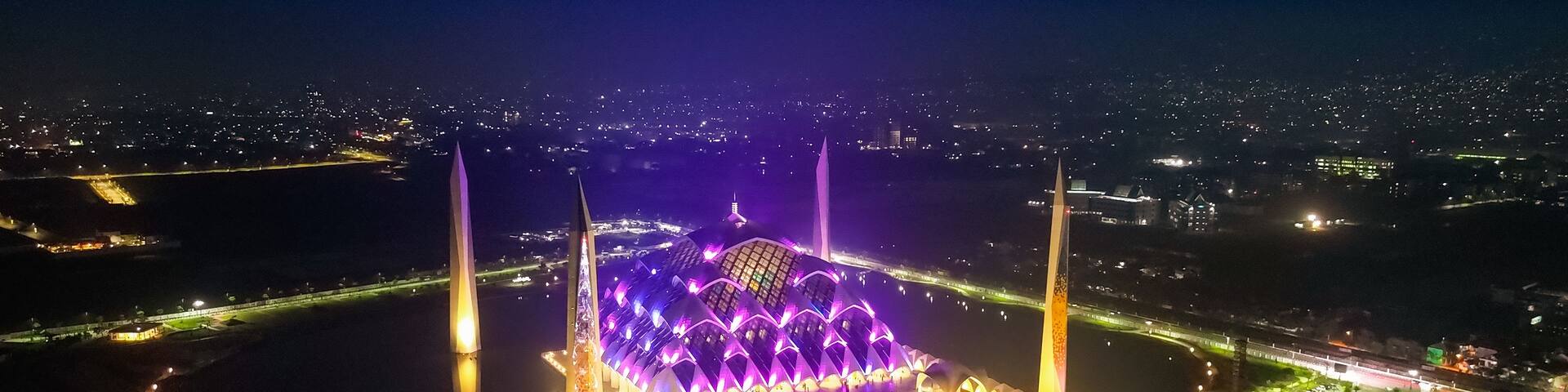A brightly lit stadium with a unique architectural design, surrounded by a body of water and illuminated pathways.