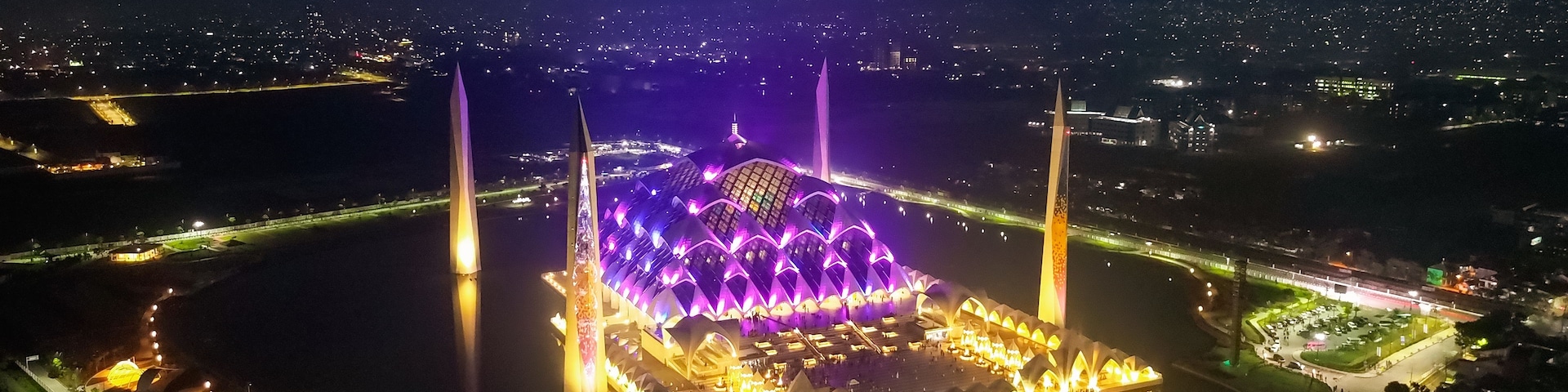 Estádio bem iluminado, com design arquitetônico singular, cercado por um corpo d'água e caminhos iluminados.
