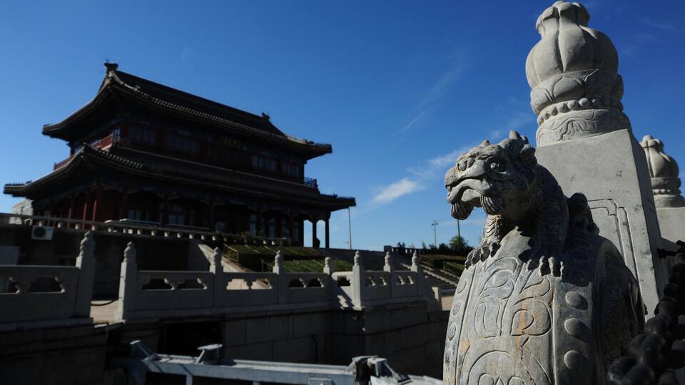 A traditional building with a tiled roof and a stone lion statue in front.
