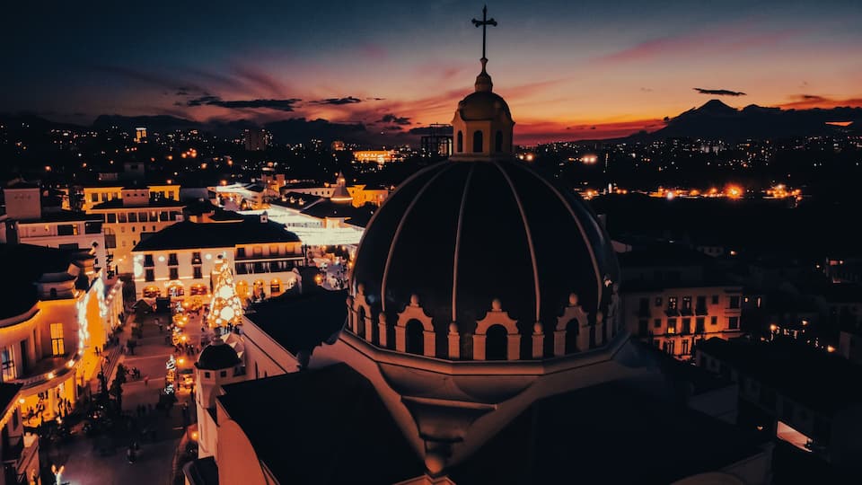 A cityscape at dusk with a prominent church dome and surrounding buildings.