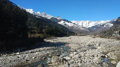 A river with large rocks, snow-capped mountains, and dense forest.