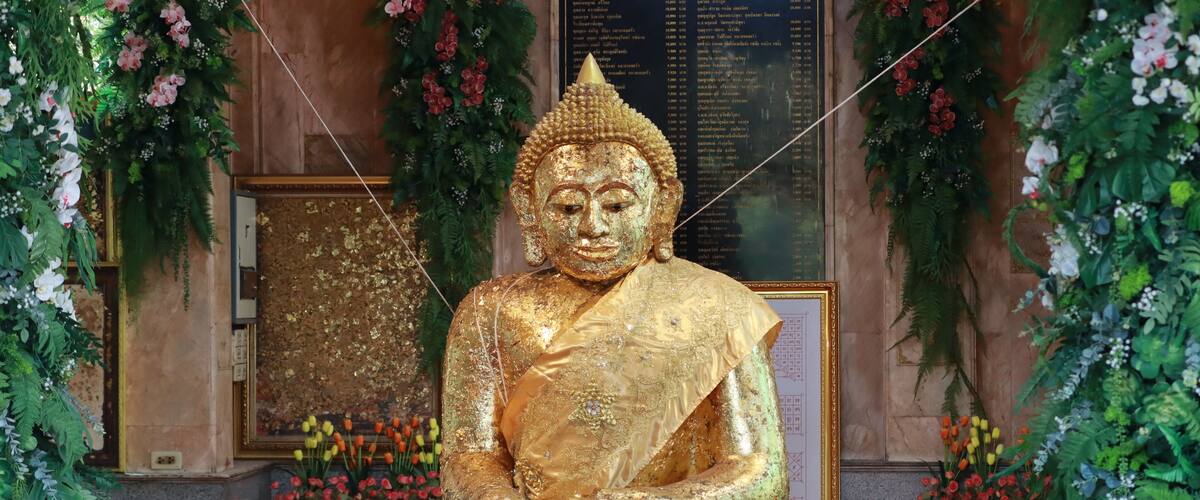 A large golden Buddha statue surrounded by floral decorations and a crowd of people.