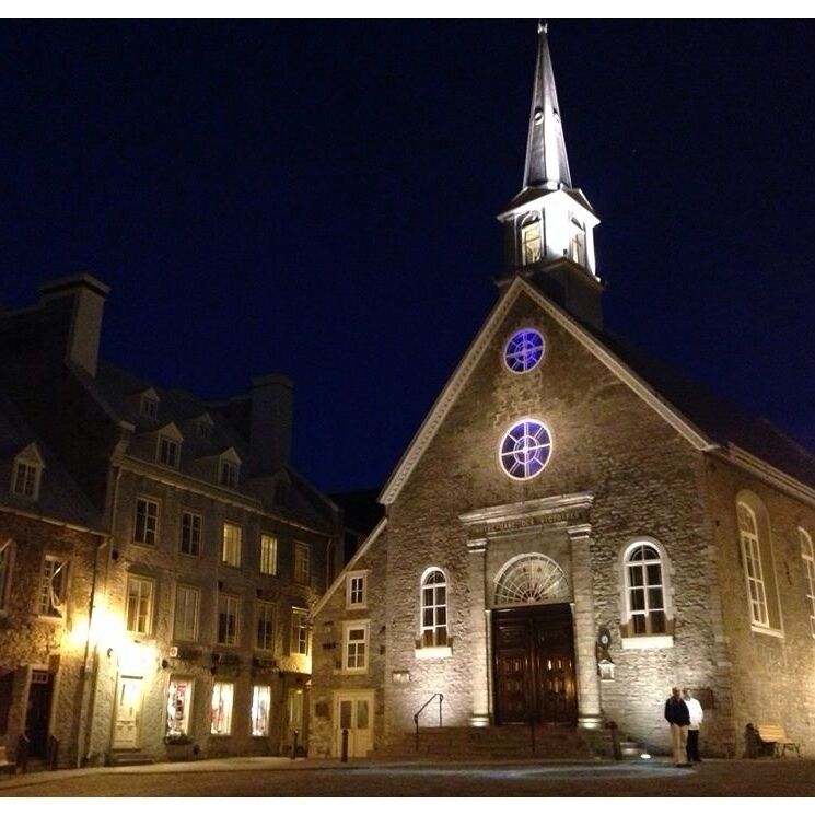 A historic stone church with a tall steeple and circular stained glass windows at night.