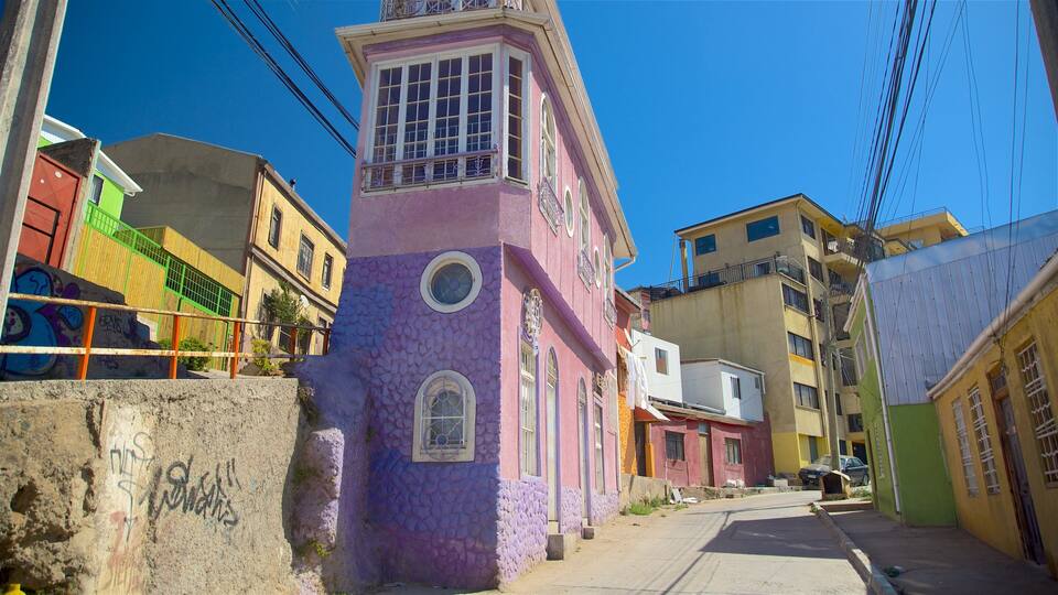 A narrow street with colorful buildings, including a pink tower with a balcony and a green building with a white door.