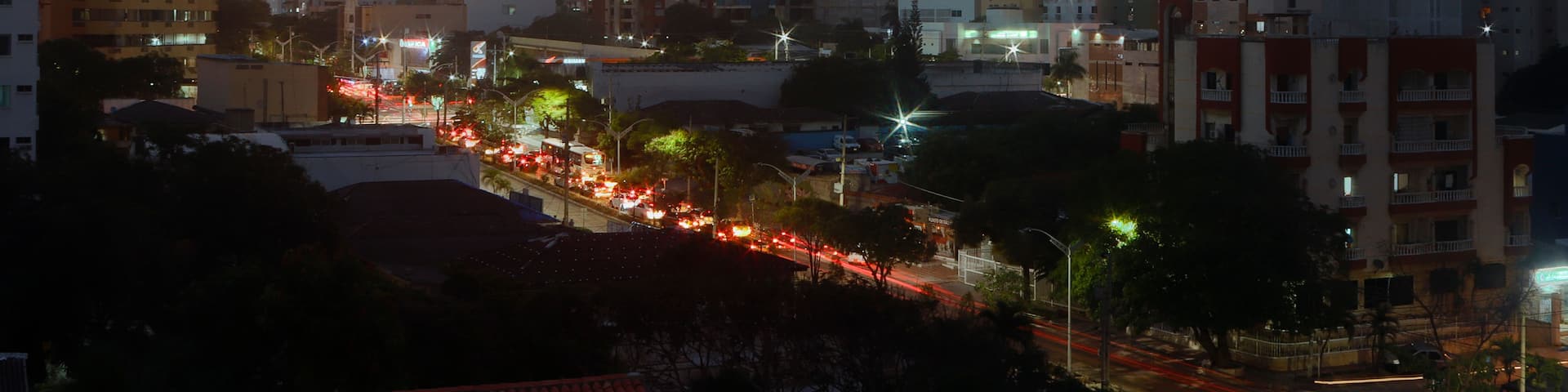 A cityscape at dusk with a sunset sky, buildings, and a busy street with light trails from vehicles.