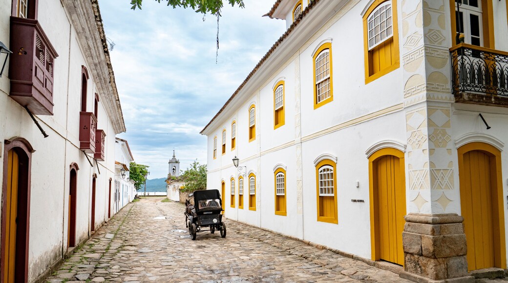 An empty historic cobblestone street featuring white colonial buildings with bright yellow windows and a horse-drawn carriage in Paraty, Brazil.