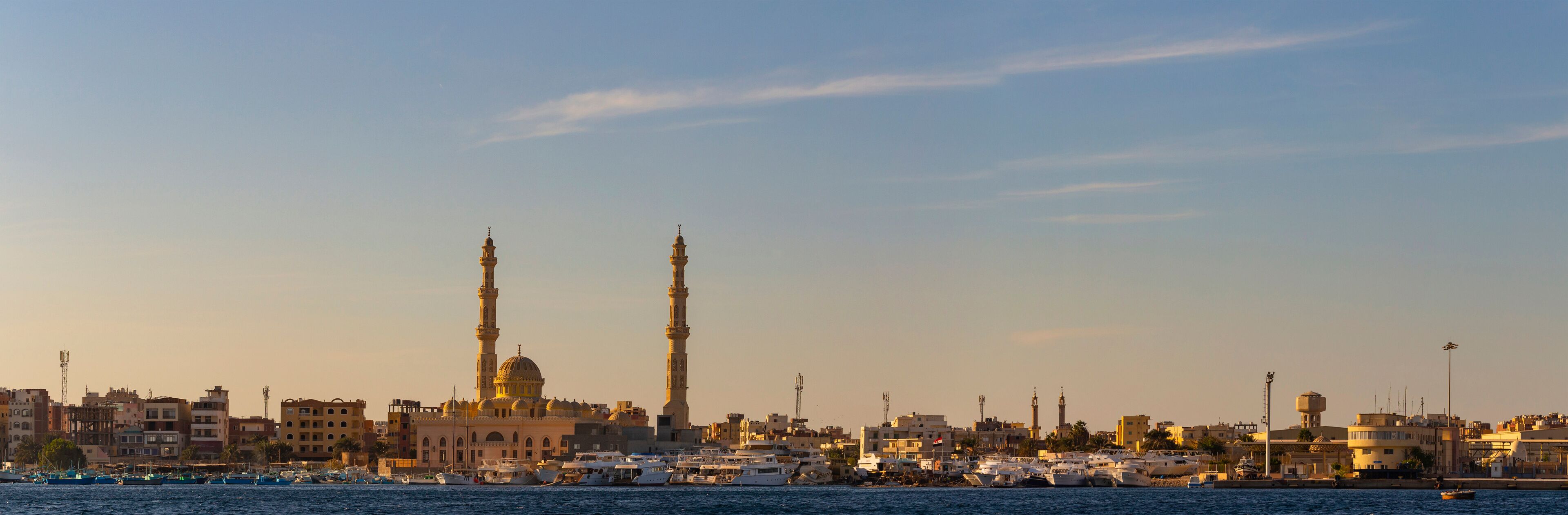 Hurghada, Egypt, a city at sunset. View of the ancient city from the red sea. Panoramic view. A port with ships and a residential area with a mosque.
