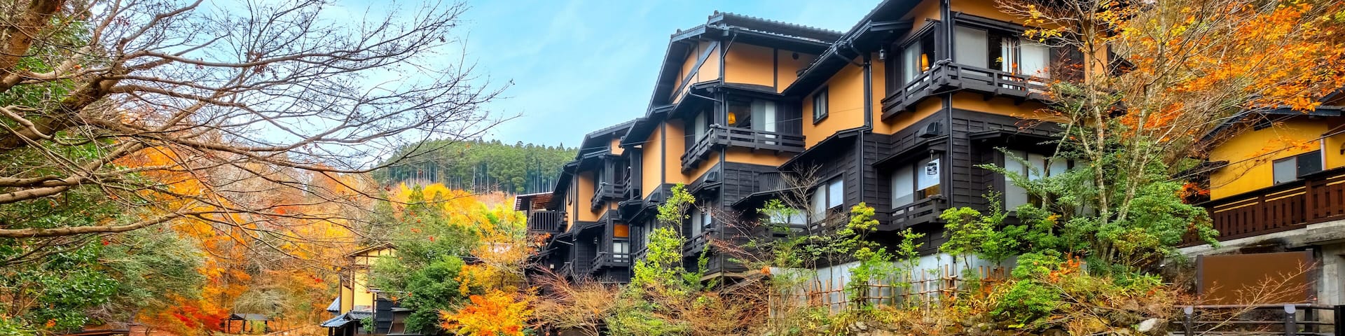 A traditional Japanese village with a river, autumn foliage, and multi-story houses.
