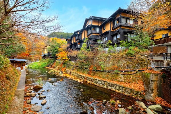 Un village japonais traditionnel, avec une riviÚre, des arbres aux couleurs automnales et des maisons à plusieurs étages.