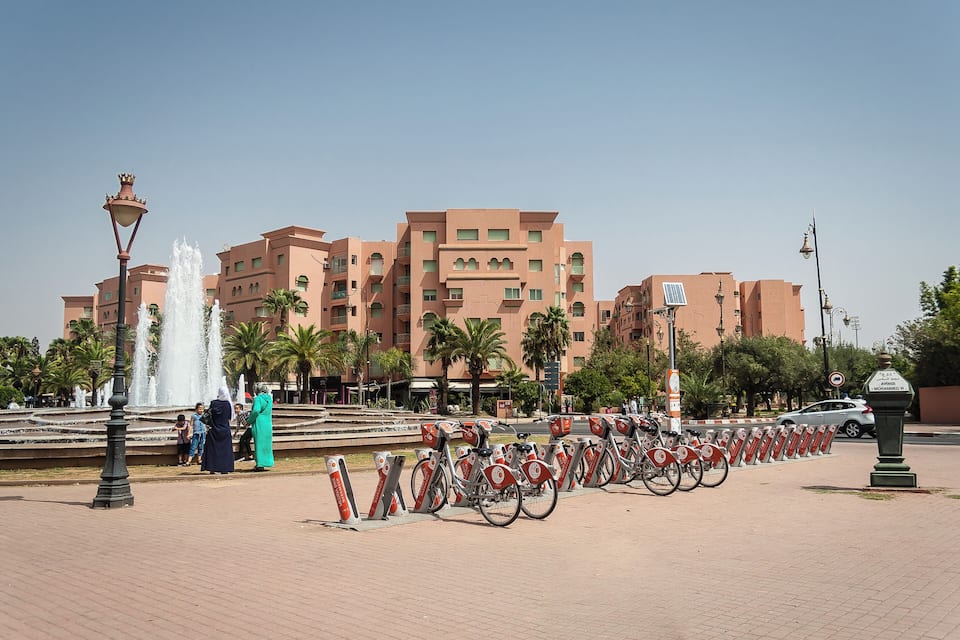 A public square with a fountain, a row of bicycles, and a large building in the background.