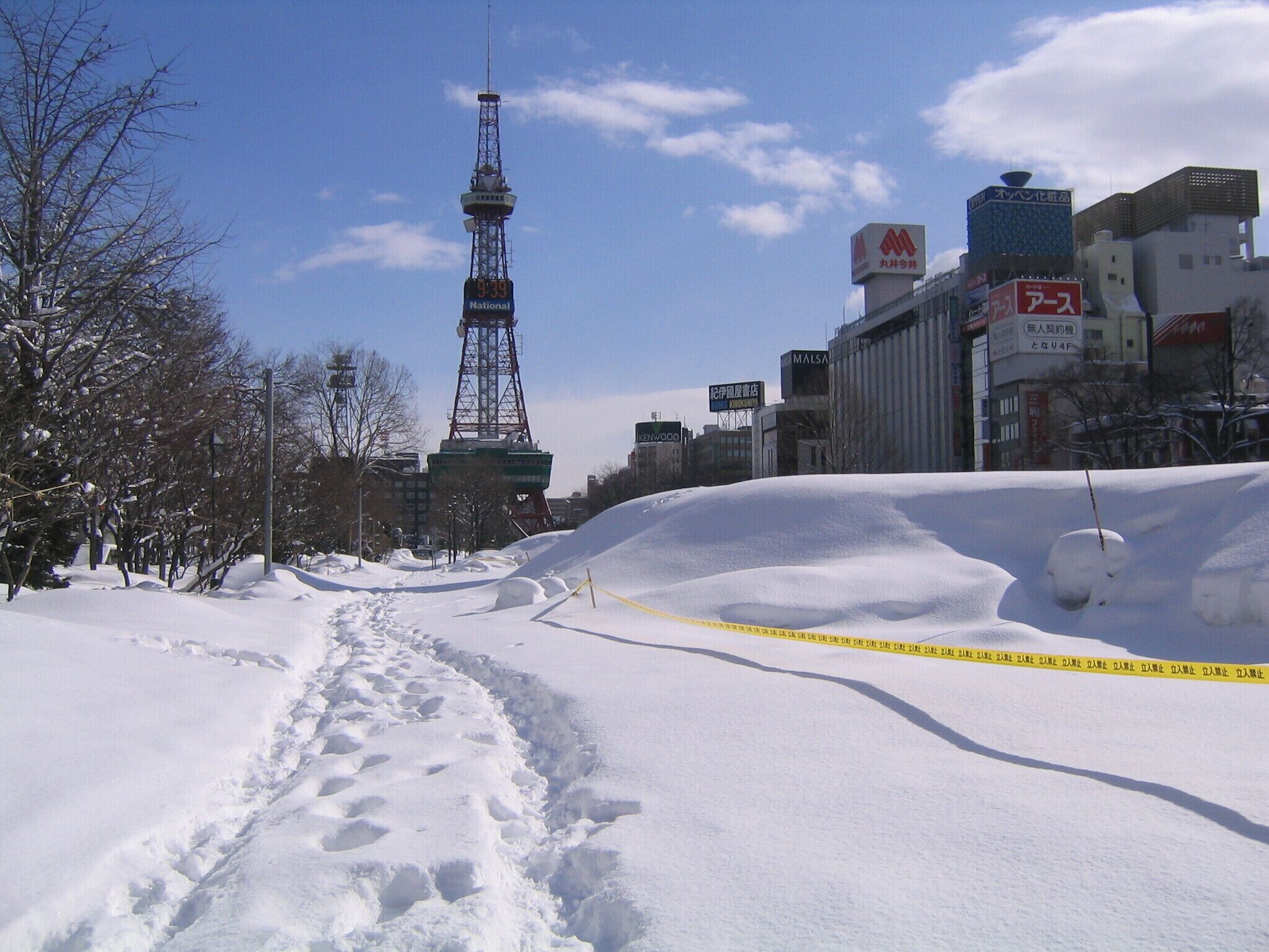 A snowy urban landscape with a prominent tower, buildings, and a yellow caution tape.